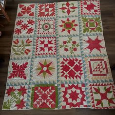 a quilt made with red and green fabric on top of a wooden floor next to a chair