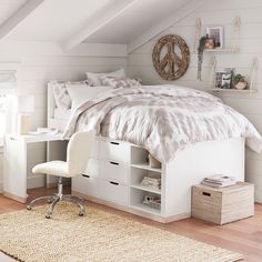 a white bed sitting under a window next to a desk and chair on top of a hard wood floor