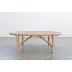 an oval wooden table sitting on top of a cement floor next to a white wall