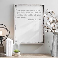 a white framed sign sitting on top of a wooden table next to a vase filled with flowers