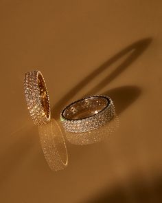 two wedding rings sitting next to each other on top of a table in front of a shadow