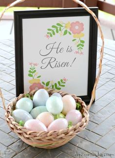 a basket filled with eggs sitting on top of a table next to a sign that says he is risen