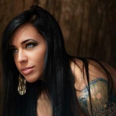 a woman with long black hair and tattoos on her arm is posing for the camera