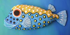 a blue and yellow painted fish sitting on top of a green surface with polka dots