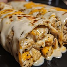 two burritos covered in cheese and chicken are on a black plate with sauce