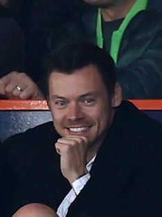 a smiling man sitting in the stands at a soccer game