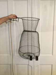 a wire basket hanging from the side of a door with a rope attached to it