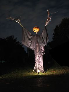 a lighted scarecrow in the dark with his arms spread out and two pumpkins on top