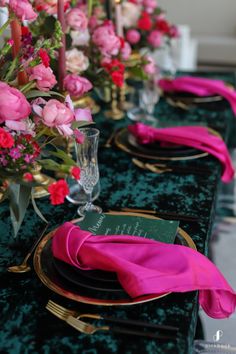 the table is set with pink flowers and gold place settings, along with green velvet napkins