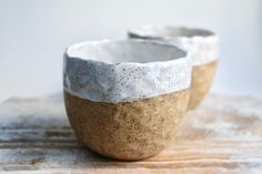 two white and brown bowls sitting on top of a wooden table