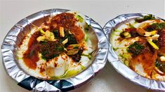 two foil plates with food on them sitting on a table