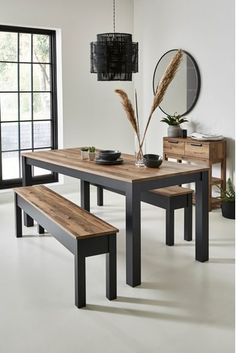 a dining room table with two benches and a mirror on the wall next to it