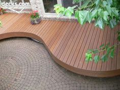 a wooden bench sitting on top of a brick patio next to a tree and potted plants