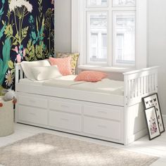 a white daybed with drawers underneath it in front of a flowered wallpaper