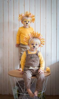 two little boys sitting on top of a table with fake flowers in their hair and wearing overalls