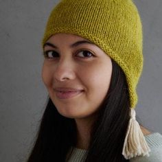 a woman wearing a yellow knitted hat with tassels on her head and smiling