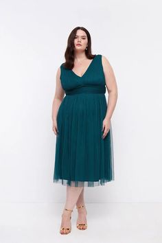 a woman in a green dress standing up with her hands on her hips and looking at the camera