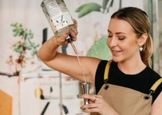 a woman in an apron is pouring something into a glass with a shaker on it