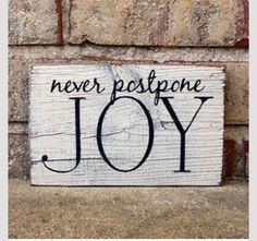 a wooden sign that says never postpone joy on the side of a brick wall