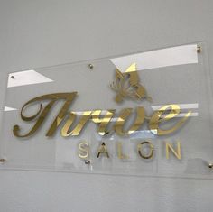 a glass sign that says three salon on the side of a white wall with gold lettering