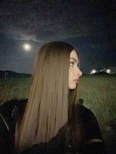 a woman with long hair standing in a field at night looking off into the distance