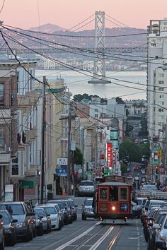 a cable car traveling down a street next to tall buildings and cars on the road