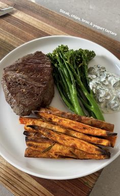 a white plate topped with steak, asparagus and sweet potato wedges next to broccoli