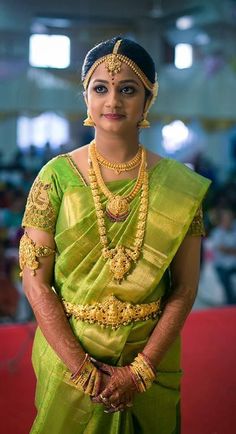 a woman in a green sari and gold jewelry poses for the camera with her hands on her hips