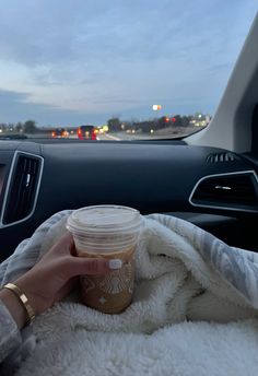 a person holding a cup in their hand while sitting in the passenger seat of a car