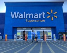 a man riding a bike in front of a walmart supercente store on a sunny day