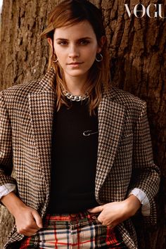 a woman standing in front of a tree with her hands on her hips and wearing plaid pants