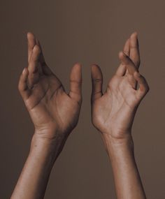 two hands reaching up towards each other with their fingers extended in the air, against a brown background