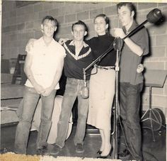 three men and one woman are standing in front of a brick wall with microphones