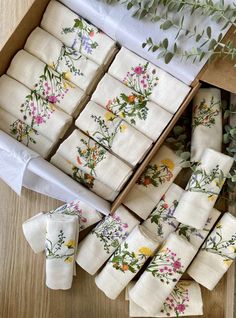 a box filled with white napkins covered in floral embroidered fabric next to a plant