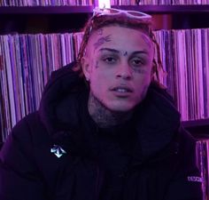 a man with tattoos and piercings on his face sitting in front of a record shelf