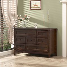 a wooden dresser with flowers and candles on it in front of a window overlooking the outside