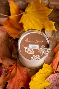 an autumn leaves candle sits on the ground surrounded by fallen leaves and fall colored leaves