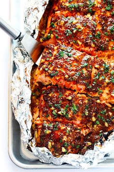 two pieces of meat covered in sauce and garnished with parsley on aluminum foil