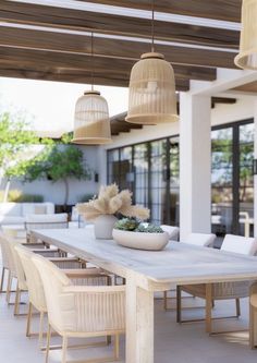 an outdoor dining area with large wooden table and white wicker chairs, potted succulent plant on top