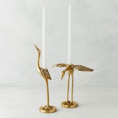 two gold flamingo candlesticks sitting next to each other on a white surface