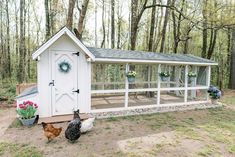 a chicken coop in the middle of a yard with chickens and flowers on the ground