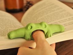 a hand is touching an open book with a green frog figurine on it