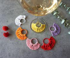 four pairs of tasseled earrings next to a glass of wine and greenery