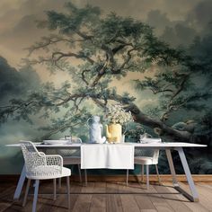 a dining room table with two chairs and a vase on it, in front of a wall mural