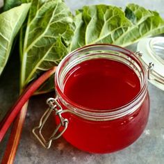 a glass jar filled with red liquid next to some green leafy vegetables on a table