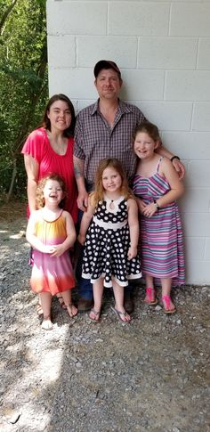 a family poses for a photo in front of a white brick wall with trees behind them