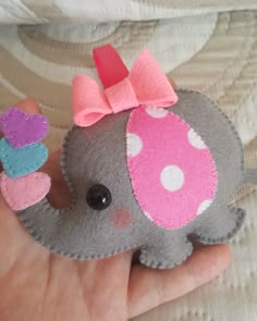 a hand holding an elephant with a pink bow on it's head and a cupcake in its trunk