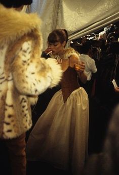 a woman in a dress and fur coat standing next to other people on an airplane