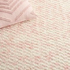 a pink and white rug on top of a bed with a pillow next to it