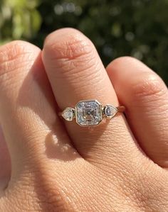 a woman's hand holding an engagement ring with three stones on the middle and one stone in the middle